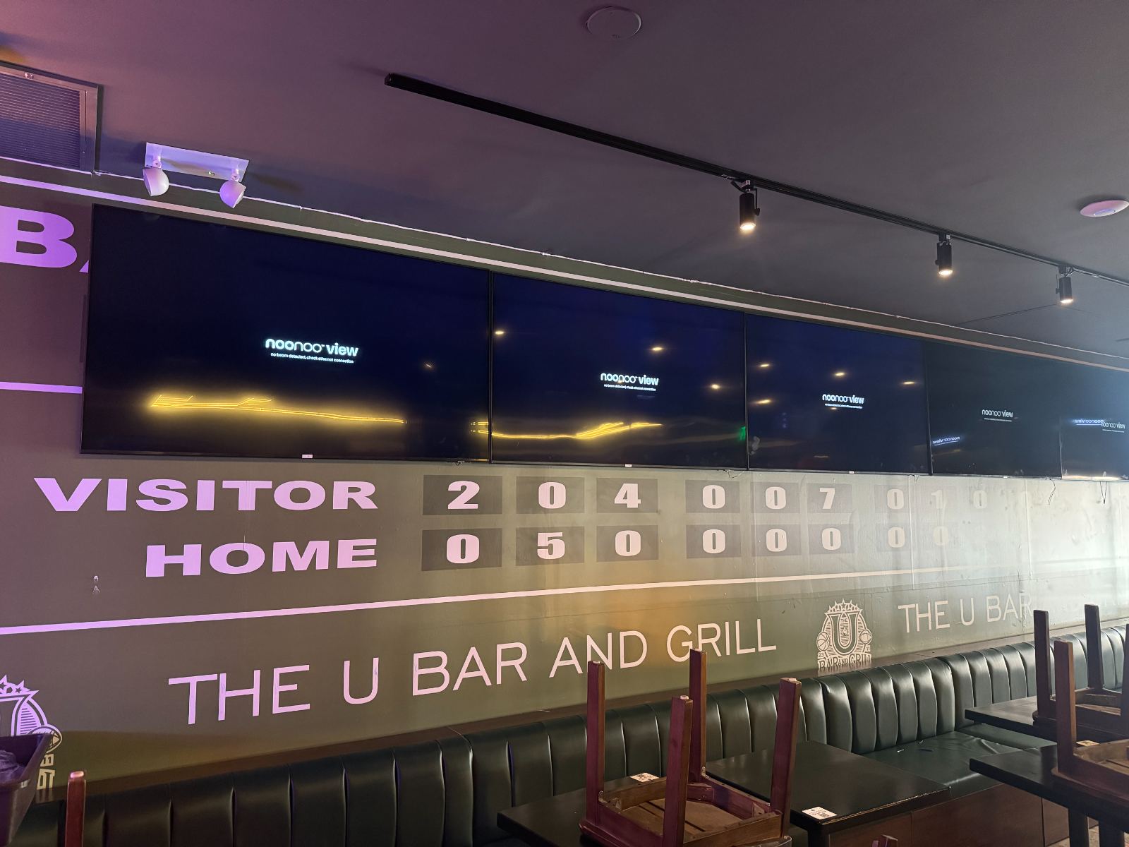A wall-width display running a live scoreboard above the booths of a bar