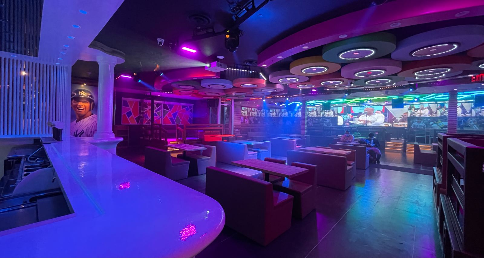 A sports lounge under violet show lighting with screens ringing the room