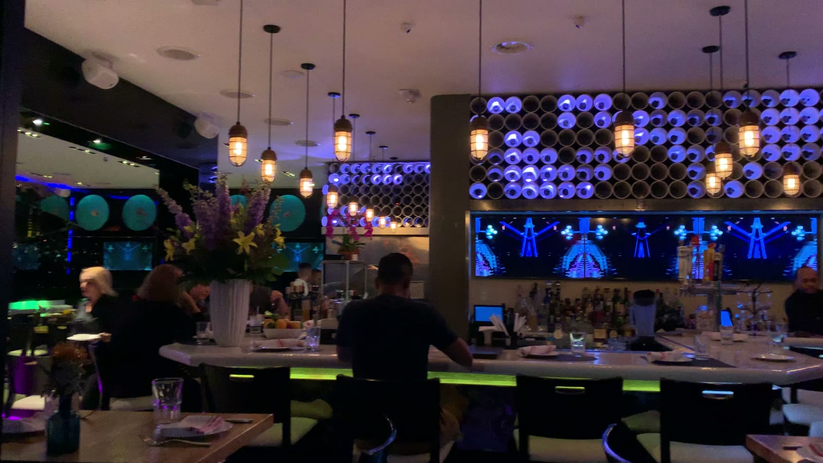 The dining room full, with the bar's lit feature wall behind it
