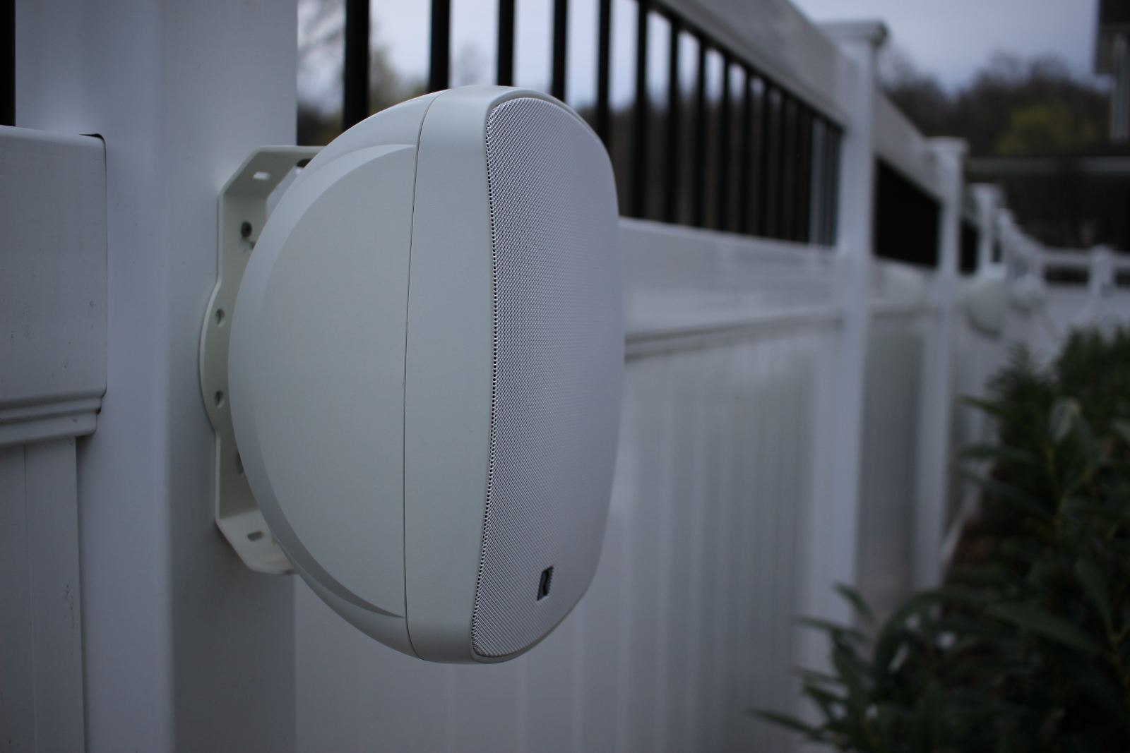 An outdoor speaker mounted along a garden fence